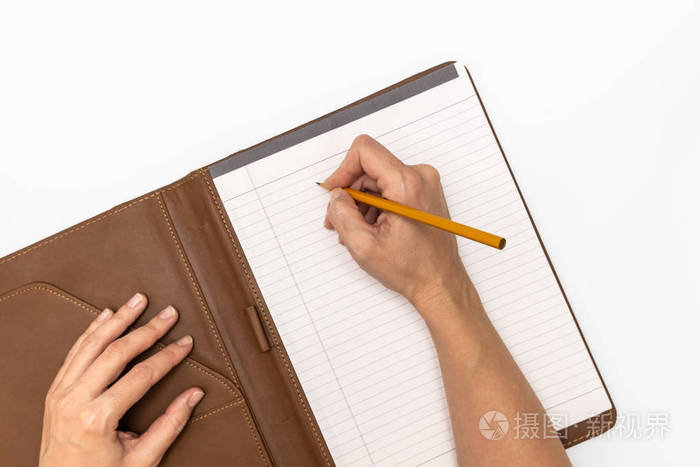 女人手拿着一本带皮封面的笔记本和一支黄色铅笔写字,特写俯视图照片