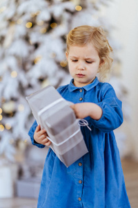 在圣诞树旁拿着圣诞礼物的小女孩