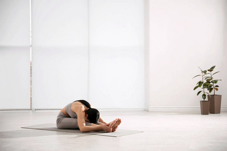 年轻女子在瑜伽室练习坐姿前弯体式。