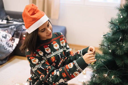 戴圣诞帽的女孩用圣诞玩具装饰圣诞树