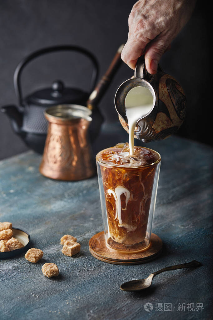 蓝灰色背景冰咖啡一只手拿着罐子往玻璃杯里倒牛奶咖啡里有美丽的牛奶