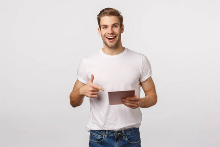 笑容可掬的金发白种男同事,穿着t恤衫,牛仔裤,手持数码平板电脑和指点