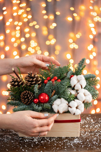 女人在一个质朴的木箱里装饰一小串新鲜云杉。圣诞气氛。花环的装饰，背景上的灯光。