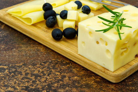 在木板上放橄榄和迷迭香的切片奶酪。葡萄酒奶酪开胃菜