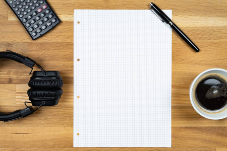 一个空的记事本，一支笔，一个计算器，一杯咖啡和一个耳机放在一张木桌上
