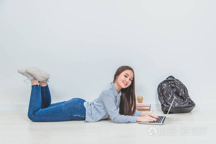 可爱的亚洲年轻女士趴在地板上在网上搜索对着镜头微笑她身边的学校