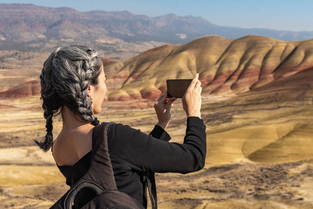 一位头发灰白的黑发年轻女子在画山俯瞰处用智能手机拍照