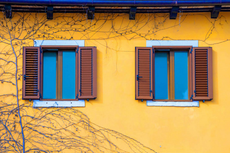 Yellow facade of a house with windows with brown shutters. 