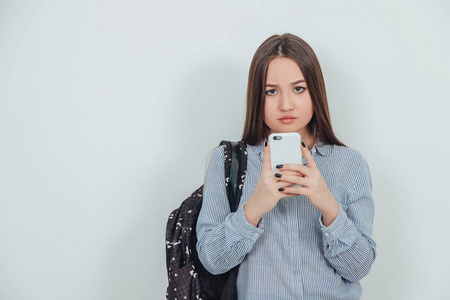 可爱的亚洲学生女孩拿着手机好像在拍照,摆姿势.背负在她的肩上.