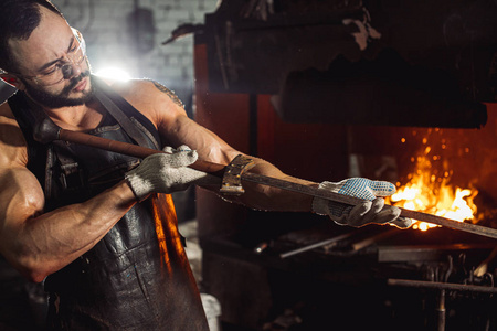 年轻的白人铁匠在铁匠铺的铁砧上锻造熔化的金属，看看它
