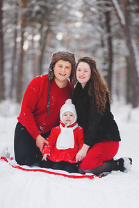 时尚的年轻家庭在冬天的雪林里玩得很开心。妈妈，爸爸和女儿坐在格子布上