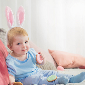 漂亮的小男孩戴着兔子耳朵，在床上放着复活节彩蛋