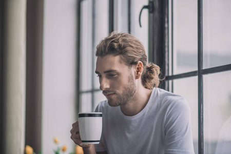 一个英俊的长头发男人喝着早晨的咖啡。