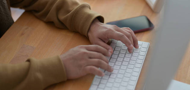 Closeup view of young man typing on keyboard computer while wor