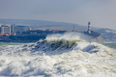 美丽的，巨大的风暴波在Gelendzhik海湾的入口处。背景是陡峭陡峭河岸上的灯塔塔。