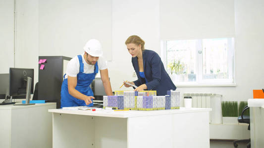 Builder and woman discuss models of houses, they rearrange house