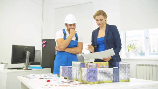 Woman stands with builder and shows something on model of house 