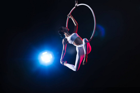 Young woman performing acrobatic element on aerial ring against 