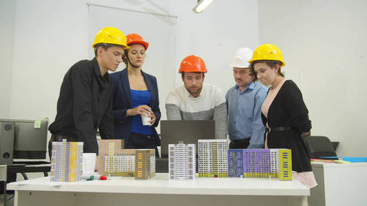 Architects in helmets look at computer and discuss a project and