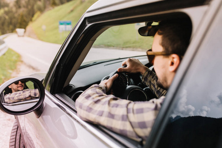 一个黑发男人开车沿着马路,仔细地看着后视镜.