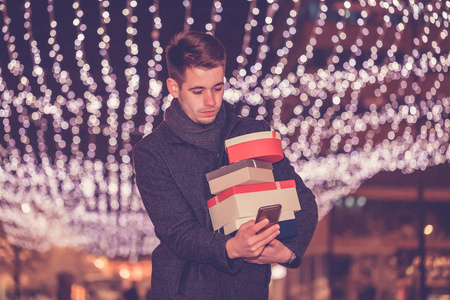 Handsome young man using smartphone and  holding presents while 