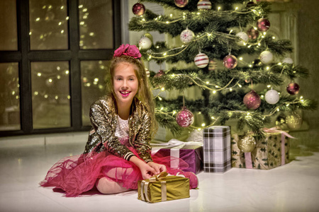 可爱的小女孩拿着礼物在圣诞树旁微笑