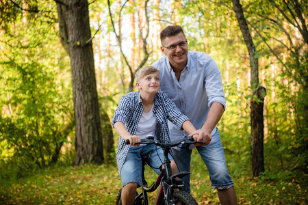兴奋的父亲和儿子一起在绿色公园玩得很开心，教儿子怎么骑自行车