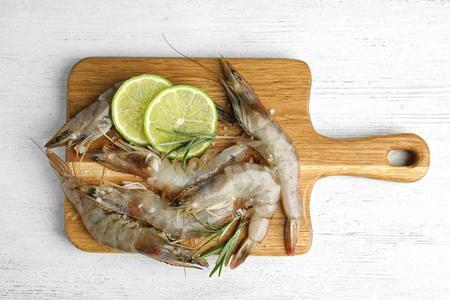 Fresh raw shrimps with lime slices and rosemary on white wooden 