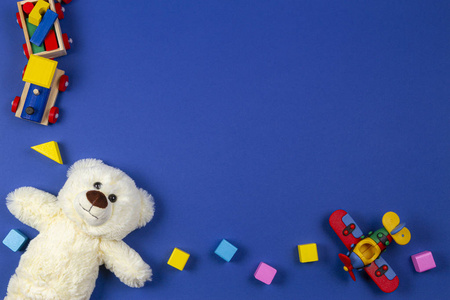 婴儿玩具背景。木制火车，泰迪熊，塑料飞机和海军蓝背景的彩色木块。俯视图