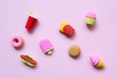 各种各样的玩具快餐和不同的糖果，在柔和的粉红色背景上有阴影。