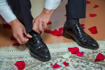 穿西装穿棕色鞋子的人。手和鞋特写。男人手系着漂亮优雅的鞋子的特写镜头。结婚日。新郎系鞋带