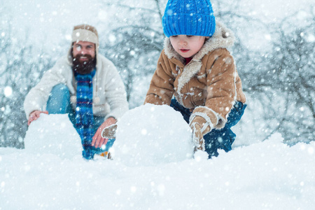 圣诞快乐，新年快乐。快乐的父子在雪地里堆雪人。手工制作搞笑雪人。