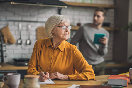 Elegant goodlooking greyhaired woman in yellow shirt looking t