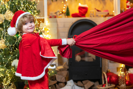 圣诞老人助手提着装满礼物的大袋子。圣诞老人助手拿着一个装有礼物的红色袋子。圣诞夜梦幻般的幼儿。圣诞老人助手。