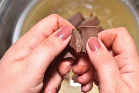 女孩的手正在把巧克力弄碎,让它热起来变成液态巧克力.特写照片