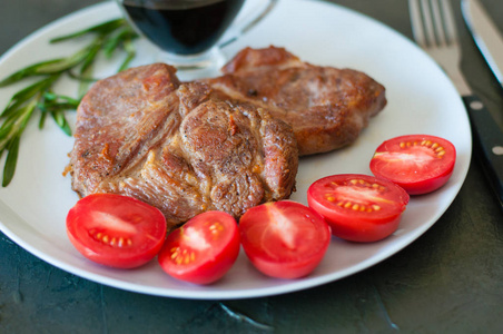 香喷喷的猪肉牛排，加上香料西红柿和酱汁，放在灰色的盘子里，在深色的混凝土背景上，特写