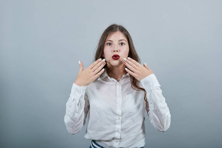 震惊的女人张开嘴指着脸颊，看着摄像机