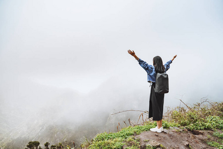 背着背包的年轻女游客在山顶上放松，欣赏雾谷的景色