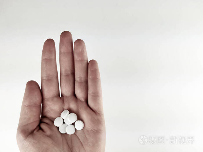 一个手掌的俯视图在白色的背景上放着许多白色的药片作为止痛药