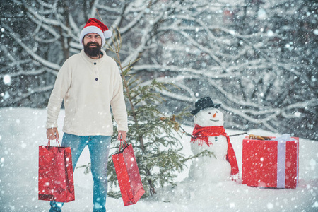 快乐的父亲在冬天雪人的背景下带着圣诞礼物。冬天的情感。英俊的圣诞老人。圣诞节冬天人们的肖像。