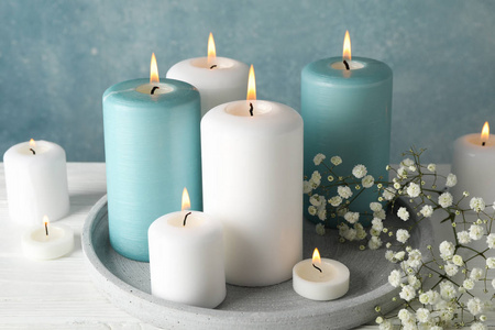 Burning candles, tray and flower against blue background, close 