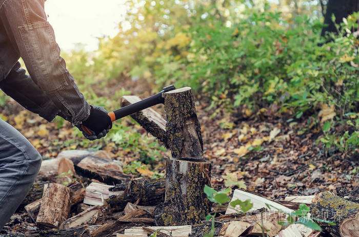 树的一部分飞开了.一个强壮的人手里拿着一把斧头,背景是森林,柴火.
