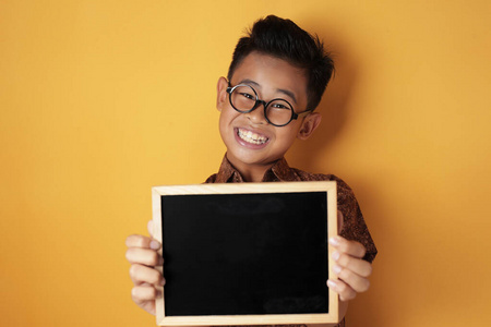 聪明的亚洲男孩对着镜头微笑，展示着空黑板
