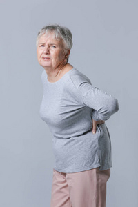 灰色背景背痛的老年妇女