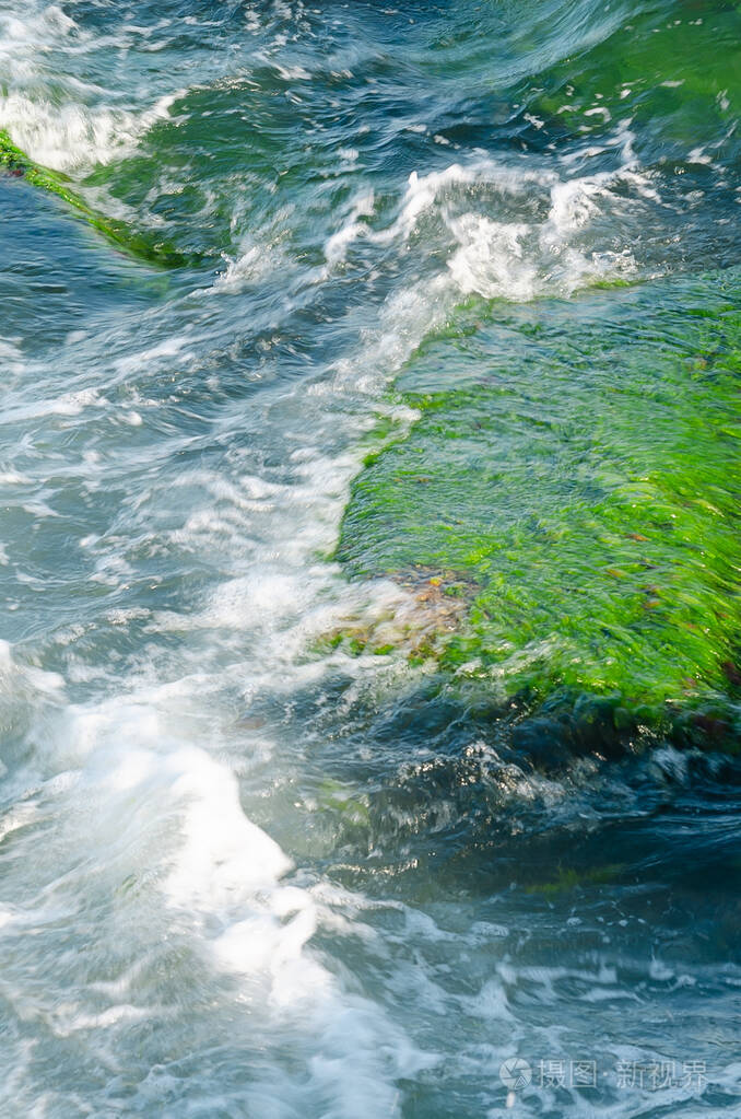 海浪拍打着覆盖着水花和泡沫的大岩石夏日特写选择性聚焦