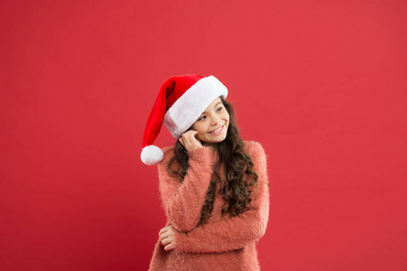 冬季传统。可爱的女孩长卷发戴圣诞老人帽红色背景。数着圣诞节前的日子。圣诞晚会。圣诞假期请柬。积极性概念。好心情
