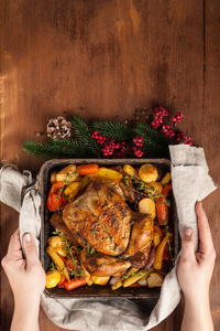 Female hands hold a baked whole chicken with vegetables. 