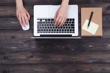 Woman working on laptop computer with notepad and pen on wooden 