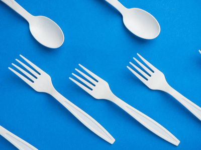 塑料白色一次性叉子和勺子在时尚的蓝色背景上。概念塑料餐具，快餐，塑料污染。俯视图，平放。