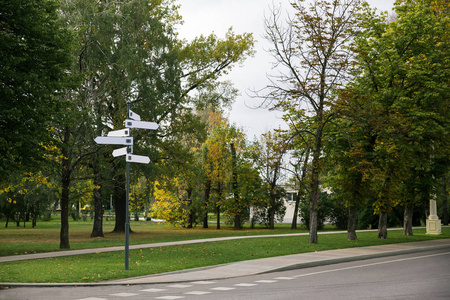 信息。城市公园道路和树木背景下的铁白色空白方向指示灯